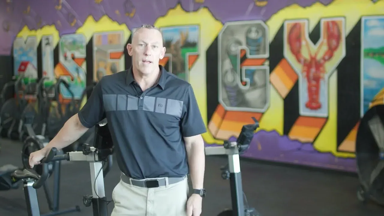 Chad standing between two bikes in front of the Misfit Gym Windham mural.