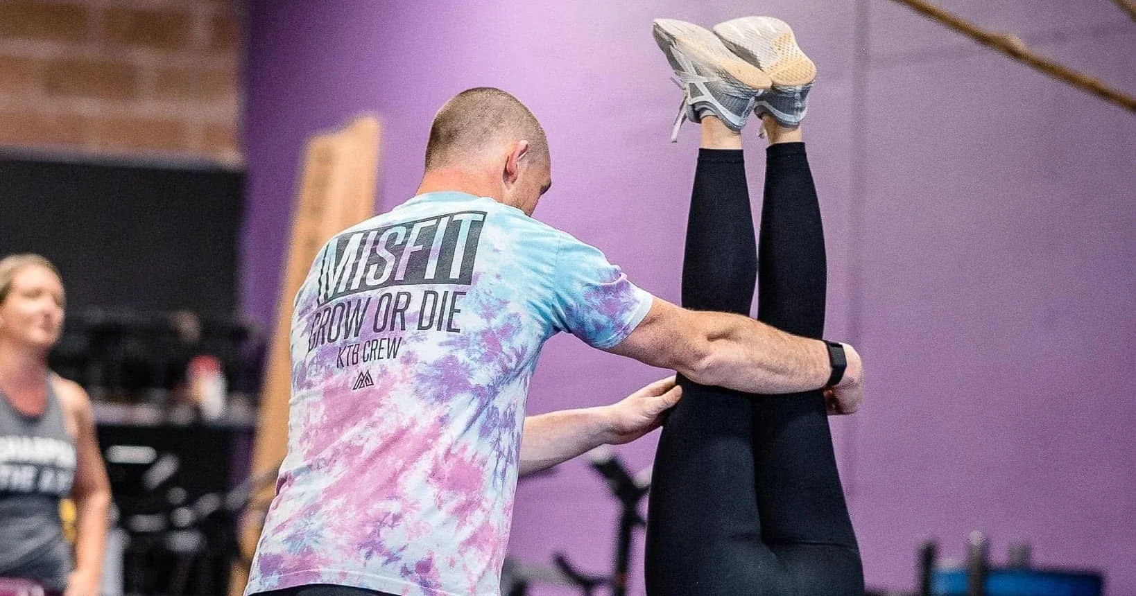 A Misfit Gym Windham coach spots a member's handstand on the gym floor, in front of the purple wall.