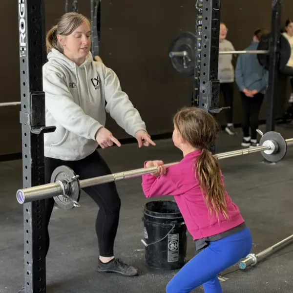 Young athlete doing a bar muscle-up while coach observes at Misfit Gym