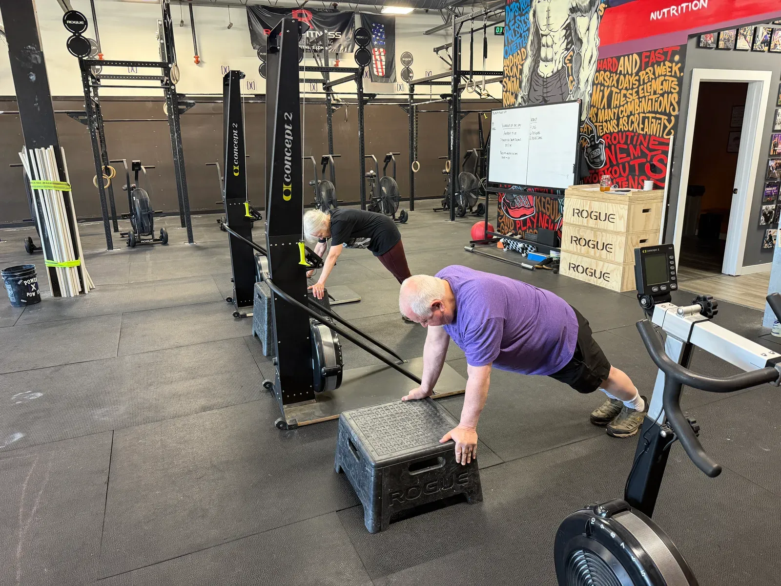 Two Misfit Gym Windham members holding a push-up position scaled to their level, one on a rower handle and one on a Rogue box.